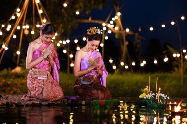 Loi Krathong Festivali, nehir kenarında salda bekleyen iki Taylandlı kadın, geleneksel Tayland kostümlü Asyalı kadınlar, Loi Krathong Günü 'nde yüzmek üzere kramponlar getiriyor, Tayland gelenekleri ve kültürü.,