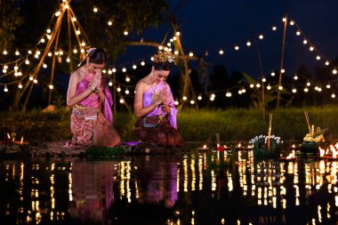 Loi Krathong Festivali, nehir kenarında salda bekleyen iki Taylandlı kadın, geleneksel Tayland kostümlü Asyalı kadınlar, Loi Krathong Günü 'nde yüzmek üzere kramponlar getiriyor, Tayland gelenekleri ve kültürü.,
