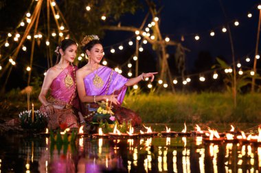 Loi Krathong Festivali, nehir kenarında salda oturan iki Taylandlı kadın, geleneksel Tayland kostümlü Asyalı kadınlar, Loi Krathong Günü 'nde yüzmek üzere kramponlar getiriyor, Tayland gelenekleri ve kültürü.,