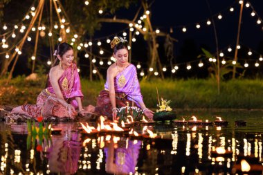Loi Krathong Festivali, nehir kenarında bir salda oturan iki Taylandlı kadın, geleneksel Tayland kostümlü Asyalı kadınlar, Tayland gelenek ve kültüründe, Loi Krathong Günü 'nde yüzmek üzere kratonglar getiriyor.,