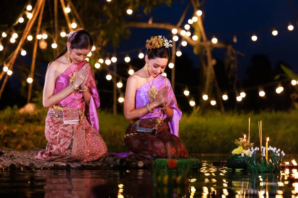 Loi Krathong Festivali, nehir kenarında salda bekleyen iki Taylandlı kadın, geleneksel Tayland kostümlü Asyalı kadınlar, Loi Krathong Günü 'nde yüzmek üzere kramponlar getiriyor, Tayland gelenekleri ve kültürü.,