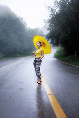 Yağmur mevsiminde yolun ortasında ayakta duran ve umblella tutan genç kadın portresi, doğal orman ve konsept.. 