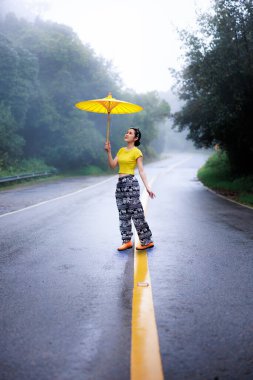 Yağmur mevsiminde yolun ortasında ayakta duran ve umblella tutan genç kadın portresi, doğal orman ve konsept.. 