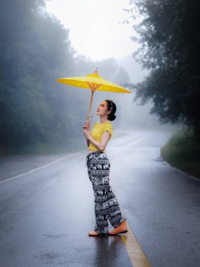 Yağmur mevsiminde yolun ortasında ayakta duran ve umblella tutan genç kadın portresi, doğal orman ve konsept.. 