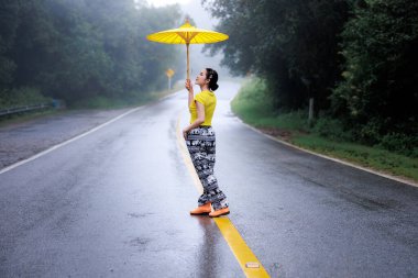 Yağmur mevsiminde yolun ortasında ayakta duran ve umblella tutan genç kadın portresi, doğal orman ve konsept.. 