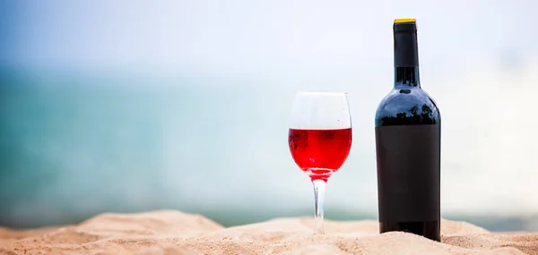 Bottle of black wine and one glasses red wine on the white sandy beach, copy space for background,
