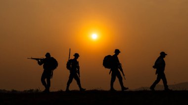 Gün batımında yürüyen ve silah tutan özel kuvvetlerden oluşan siluet grubu ve renkli turuncu gökyüzü geçmişi, özel savaş tatbikatı timleri.