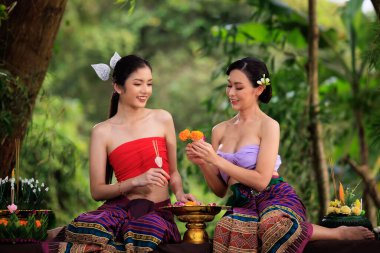Antik Tayland elbisesi giymiş genç bir kadın Krathong yapmak için birbirlerine yardım eder. Doğa arka planında.