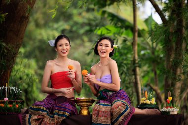 Antik Tayland elbisesi giymiş genç bir kadın Krathong yapmak için birbirlerine yardım eder. Doğa arka planında.