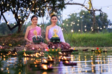 Loi Krathong Festivali, Taylandlı bir kadın nehir kenarında bir salda oturmuş krathong tutuyor, geleneksel Tayland kostümlü Asyalı kadınlar Loi Krathong Günü 'nde yüzmek için kratong getiriyor., 