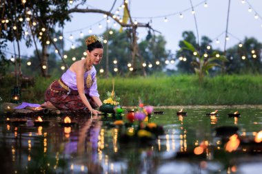 Loi Krathong Festivali, Taylandlı bir kadın nehir kenarında bir salda oturmuş krathong tutuyor, geleneksel Tayland kostümlü Asyalı kadınlar Loi Krathong Günü 'nde yüzmek için kratong getiriyor., 