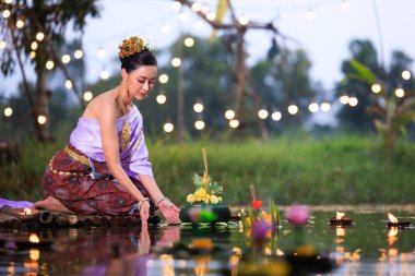 Loi Krathong Festivali, Taylandlı bir kadın nehir kenarında bir salda oturmuş krathong tutuyor, geleneksel Tayland kostümlü Asyalı kadınlar Loi Krathong Günü 'nde yüzmek için kratong getiriyor., 
