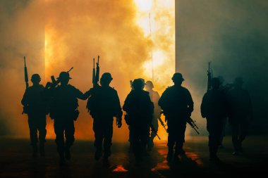 Siluet bir grup asker üniformalı özel kuvvetler. Duman ateşi altında yürüyorlar ve ellerinde silah tutuyorlar. Arka planda ışıklandırma, özel savaş tatbikatı timleri.,