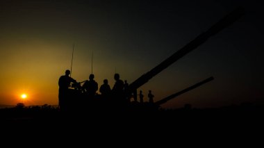 Özel kuvvetler askerlerinden oluşan siluet bir grup günbatımında arka planda bulunan tank silah kamyonuna binip oturuyorlar.
