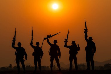 Özel kuvvetler askerlerinin siluet grubu gün batımında ve renkli turuncu gökyüzü arka planında ayakta durup silah tutuyorlar, özel savaş tatbikatı timleri