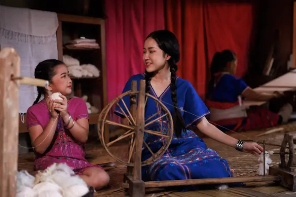 mother and daughter help each other spin yarn with traditional equipment on the balcony house,