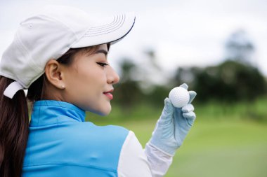 Beyaz gökyüzü arka planında golf topunu tutan Asyalı genç bayan golfçünün portresi.,