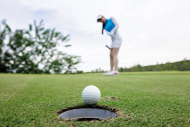 Golf turnuvasında golf oynayan profesyonel kadın golfçü, golf sahasında seçici bir şekilde golf topuna odaklanıyor.,