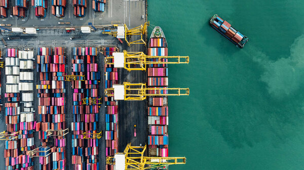 commercial port load and unloading cargo from container ship import and export by crane for distributing goods by trailers transported to customers and dealers, aerial top view photograph
