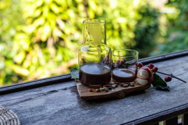 Cam bardakta sade kahve ve ahşap masada şişe ve doğal ışık arka planında çiğ chery kahve..