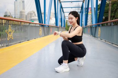 Genç bir kadın sabah koşmadan önce zaman zaman bileğindeki zamanlayıcıya bakıyor..