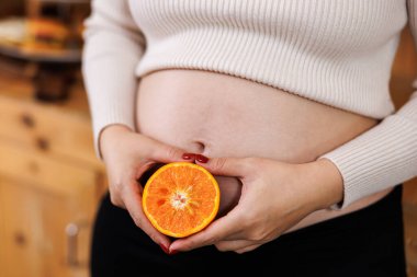 Mutfakta portakal meyvesi gösteren hamile Asyalı kadının seçici odak portresi..