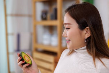 Avokado meyveleri gösteren ve elinde avokado meyveleri olan gülümseyen Asyalı kadının seçici odak portresi..