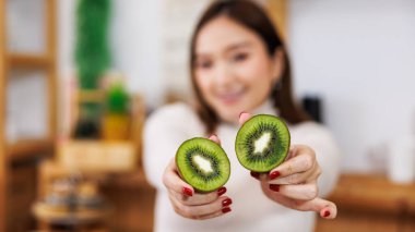 Mutfakta kivi meyveleri gösteren Asyalı hamile bir kadının gülümseyen portresi..
