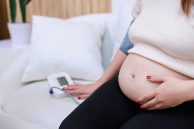 Hamile Asyalı kadın kan basıncını sfenometre cihazıyla ölçüyor..