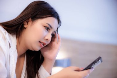 Asyalı bir kadın yatak odasındaki bir dairede yatağında telefonunda bir mesaj görünce rahatsız ve stresli olur..