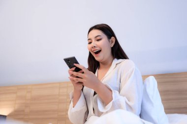 Genç Asyalı bir kadın yatak odasında akıllı telefon kullanıyor ve sabah mutlu mesut uyuyor..