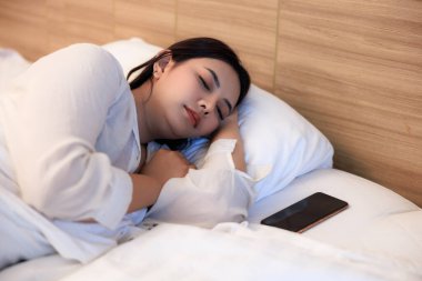 Genç Asyalı kadın yatak odasında beyaz yatakta uyuyor..