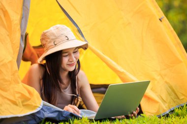 Safari elbiseli genç Asyalı kadın turist ve dizüstü bilgisayar üzerinde çalışırken sabah doğanın ortasında çadırın içinde serbest konsept olarak yatıyordu.