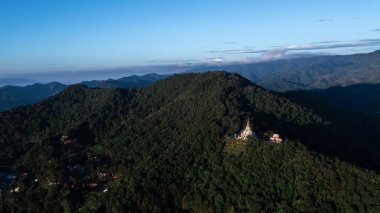 Hava manzarası, dağ sıraları ve Chiang Rai Tayland 'da sakin bir sabah sisi ile çevrili orman yamacında yuva yapmış güzel bir tapınak gösteriyor..