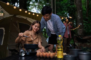 Genç Asyalı kadın ve çiftin kamp alanındaki piknik gazında ızgara et yediği yakın ve seçici bir odak noktası. Hafta sonu tatili kavramı..