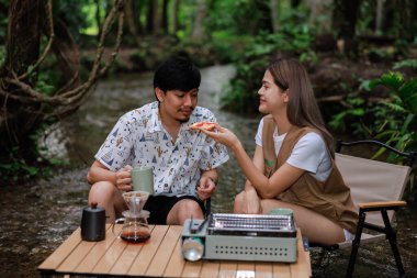 Genç bir çift iskemlede oturuyor ve derede dinleniyor. Sabahları kahve içip kadeh kaldırıyor. Kamp yapıyor, tatil konseptinde dinleniyor..