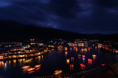 Gece sahnesinde Ban Rak Thai Köyü, renkli ışıklar ve güzel dekoratif lambalar, göldeki hareket bulanık Çin tekneleri, uzun pozlu çekim konsepti.