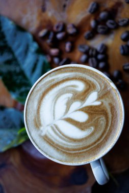 Kahve fincanı kapuçinosu ve yeşil yapraklı kavrulmuş kahve çekirdekleri ahşap masa üstü manzaralı.