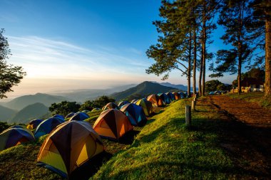 Bir dağ kamp alanının sabah manzarası. Yumuşak güneş ışığı altında birkaç çadır, açık mavi bir gökyüzü ve aşağıda bir sis denizi vardır. Bu çadır, oğlu Chiang Mai Tayland kampında huzur dolu bir güzellik hissi taşır..