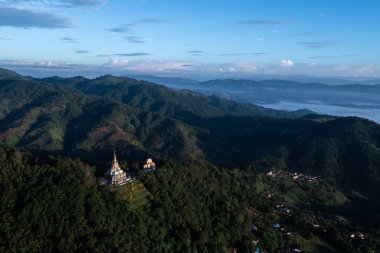 Hava manzarası, dağ sıraları ve Chiang Rai Tayland 'da sakin bir sabah sisi ile çevrili orman yamacında yuva yapmış güzel bir tapınak gösteriyor..