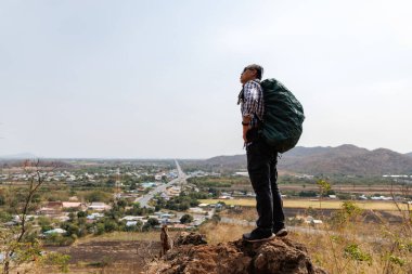 Bir erkek gezginin tepenin üstünde dikiz üstü duruşu, bir sırt çantası taşıması, ve aşağıdaki manzaraya bakması, bir yol, küçük bir kasaba ve uzak dağları kapsıyor. Bu bir macera ve keşif duygusu taşır..
