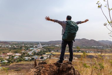 Bir erkek gezginin tepenin üstünde dikiz üstü duruşu, bir sırt çantası taşıması, ve aşağıdaki manzaraya bakması, bir yol, küçük bir kasaba ve uzak dağları kapsıyor. Bu bir macera ve keşif duygusu taşır..