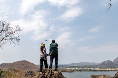Kayalık bir zirvede el ele tutuşan gezgin bir çiftin arka planda bir rezervuar, bir kasaba ve dağlar barındıran manzaraya bakışları. Bu paylaşılan bir macera ve açık hava romantizmi hissi veriyor..