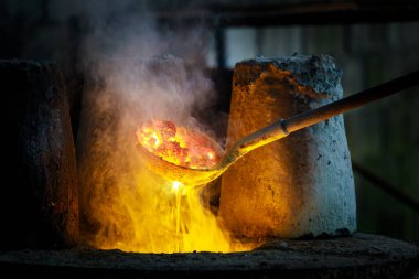 Close-up of blacksmith holding a hot crucible by the iron pliers from furnace and pouring the melting gold into the statue block