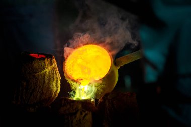 Close-up of blacksmith holding a hot crucible by the iron pliers from furnace and pouring the melting gold into the statue block