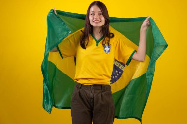 2022 Katar Kupası 'nda Brezilya futbol takımının resmi formasını giyen ve stüdyo fotoğrafında Brezilya bayrağı taşıyan bir kadın. Brezilyalı taraftar.
