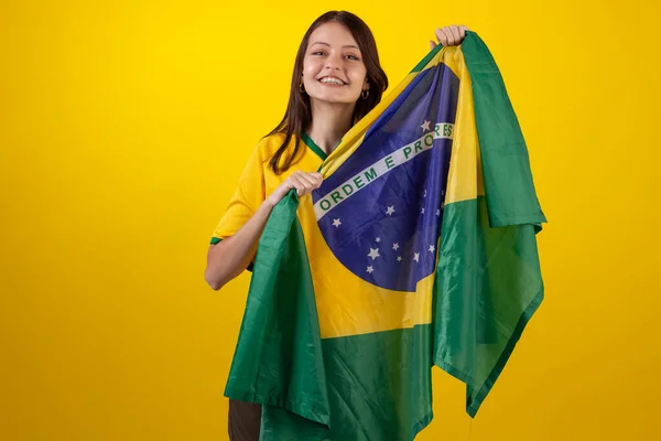 2022年のカタールカップでブラジルサッカーチームの公式ユニフォームを着た若い女性とスタジオ写真のブラジルの国旗 ブラジルのファン — ストック写真