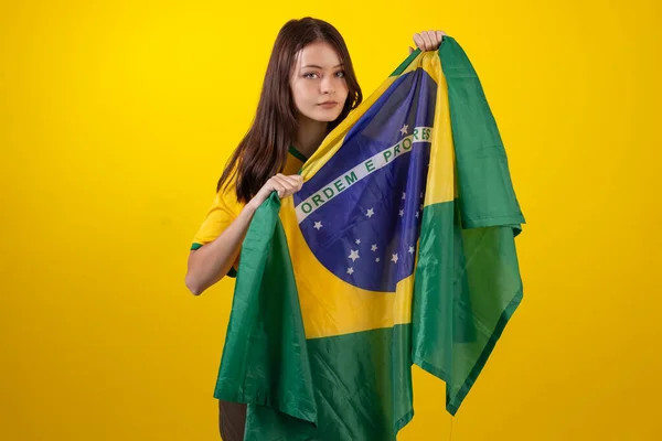 2022年のカタールカップでブラジルサッカーチームの公式ユニフォームを着た若い女性とスタジオ写真のブラジルの国旗 ブラジルのファン — ストック写真