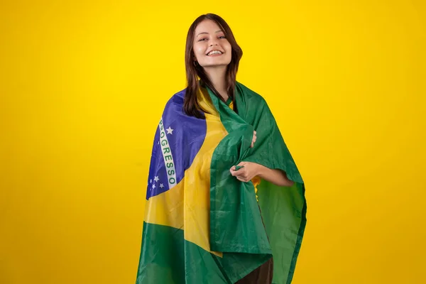oung woman wearing the official uniform shirt of the Brazilian soccer team in the 2022 Qatar Cup and with the flag of Brazil in studio photo. Brazilian fan.