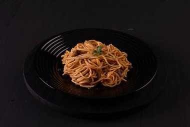 Spaghetti with sauce on a black plate in a darker studio photo.